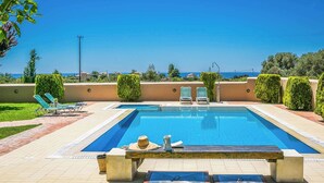 A rectangular swimming pool with a tiled deck, lounge chairs, and a table with a hat and pitcher.