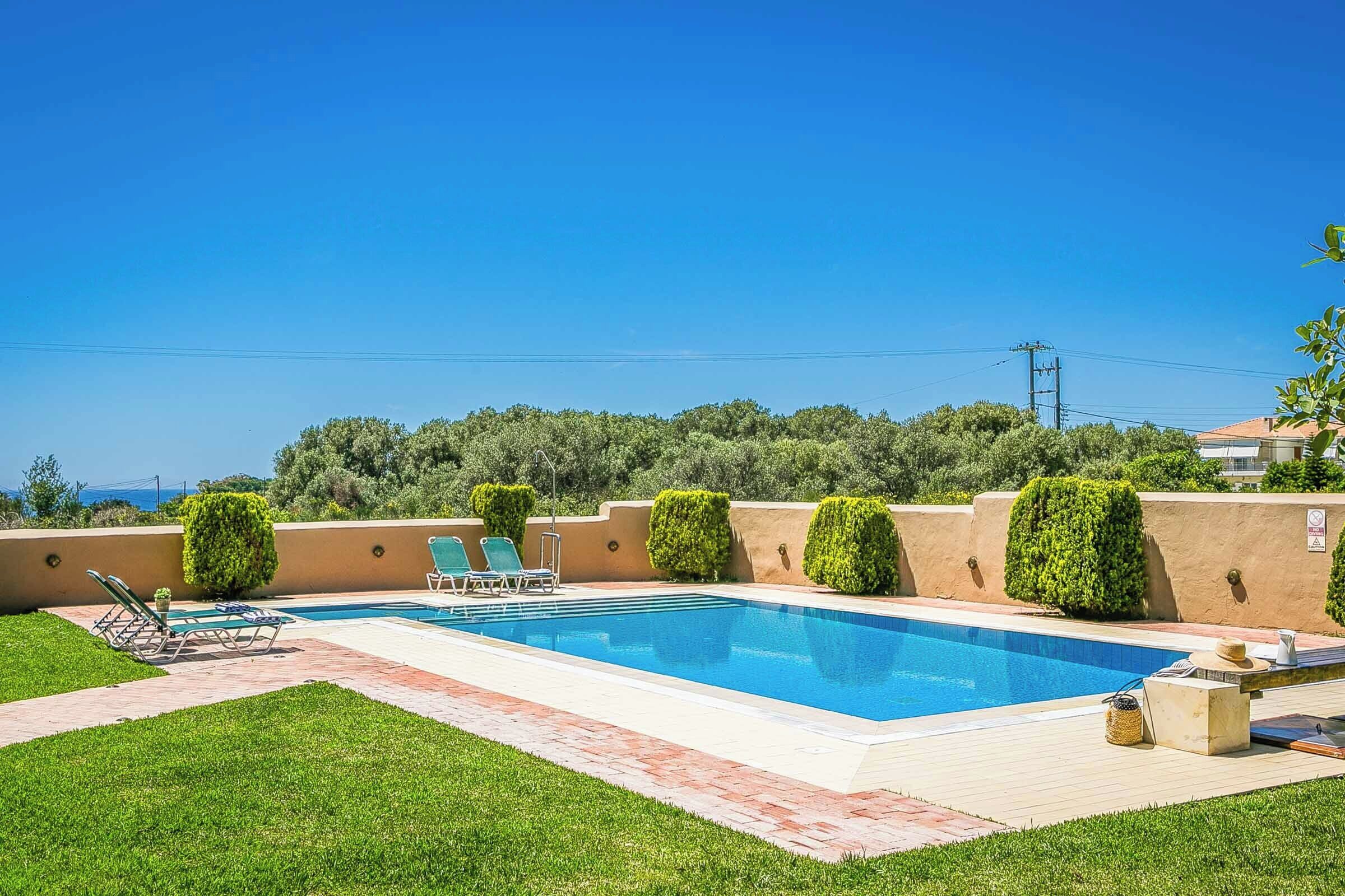 A rectangular swimming pool with a clear blue water surface, surrounded by a paved deck and a well-maintained lawn.