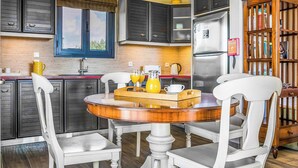 A modern kitchen with dark cabinets, a stainless steel refrigerator, and a wooden dining table with white chairs.