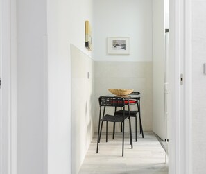 Ein schmales Entree mit einem kleinen Tisch und zwei Stühlen, einem gewebten Korb auf dem Tisch und einem gerahmten Bild an der Wand.