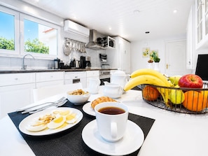 A modern kitchen with white cabinetry, a dining table set with breakfast items, and a fruit basket. - Villa Small Paradise with private pool , Jacuzzi , BBQ ,garden and privacy (Ialisos)