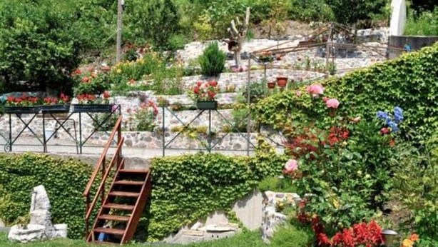 A garden with a wooden staircase, stone walls, and various plants and flowers. - Pontebba: Cozy apartment for skiing in the Alps! (Pontebba)