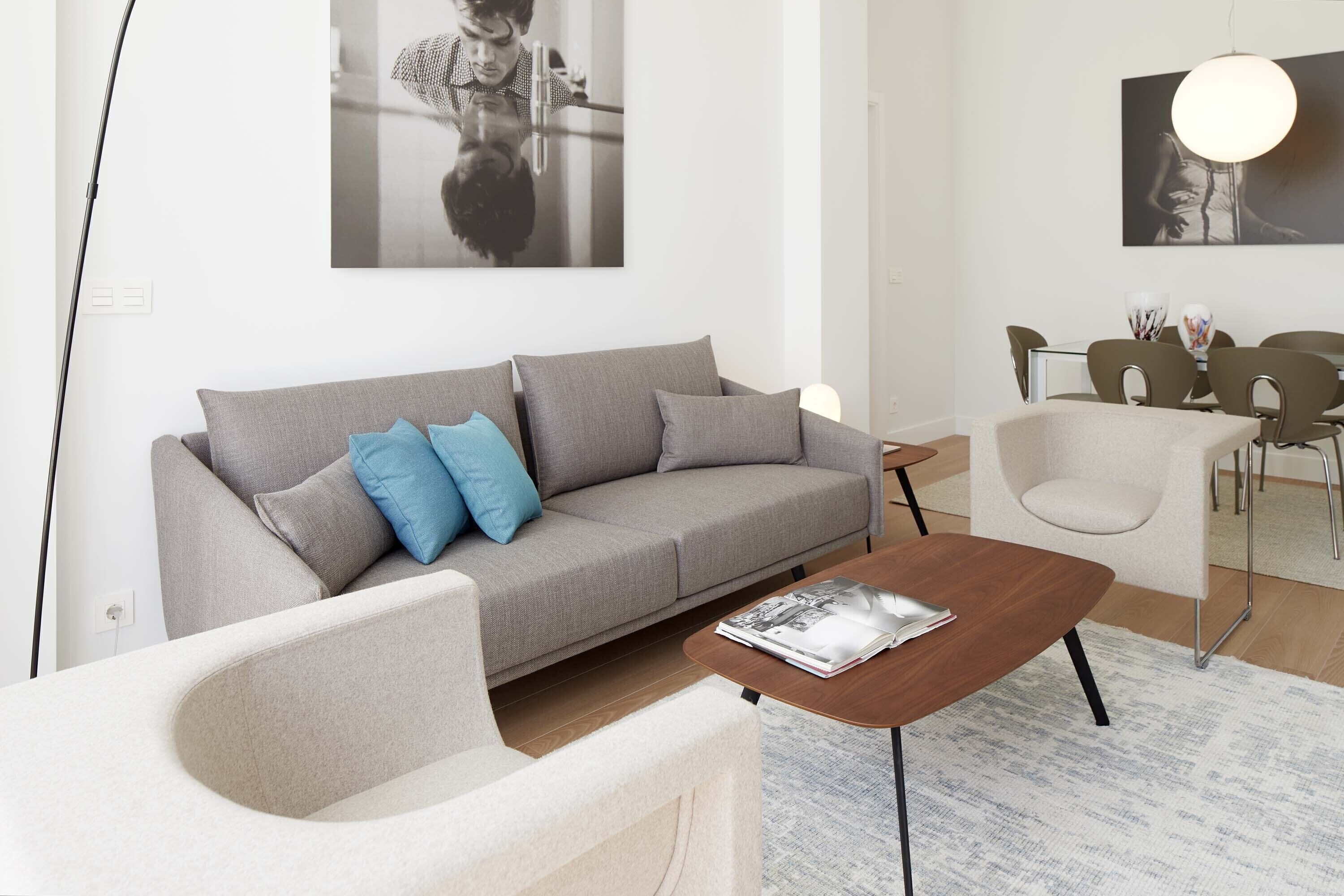A modern living room with a grey sofa, a coffee table, and a dining area with chairs and a table.