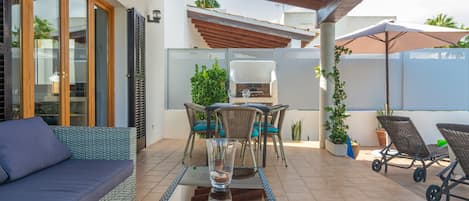 A patio area with a sofa, dining table, chairs, and a grill.
