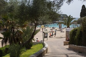 A beach with palm trees, a pathway leading to the beach, and people enjoying the area. - CASA HECTOR - Villa with private pool in Cala d'Or. Free WiFi (Santanyí)