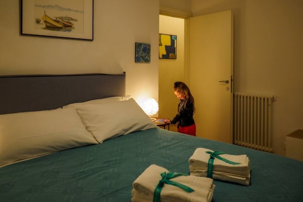 Una habitación de hotel con una cama, una mesita de noche, una lámpara y una puerta que da a otra habitación.