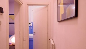 Un couloir étroit avec une porte donnant sur une salle de bain équipée d’un lavabo bleu et d’un porte-serviettes.