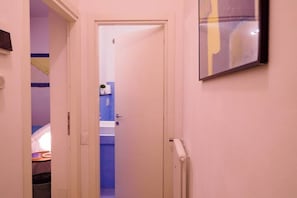 Un pasillo estrecho con una puerta que da a un baño con un lavamanos azul y un perchero.
