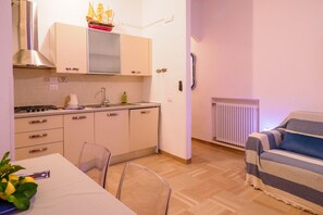 Cocina compacta con estufa, lavamanos y armarios, una mesa de comedor con sillas y un sofá a rayas en la sala.
