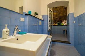 A bathroom with a white sink, blue tiles, a mirror, and a shower area with a stone wall.