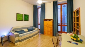 Un salon chaleureux avec un canapé à rayures, un meuble en bois, une table à manger sur laquelle se trouvent un livre et une assiette de citrons, et un ventilateur de plafond.