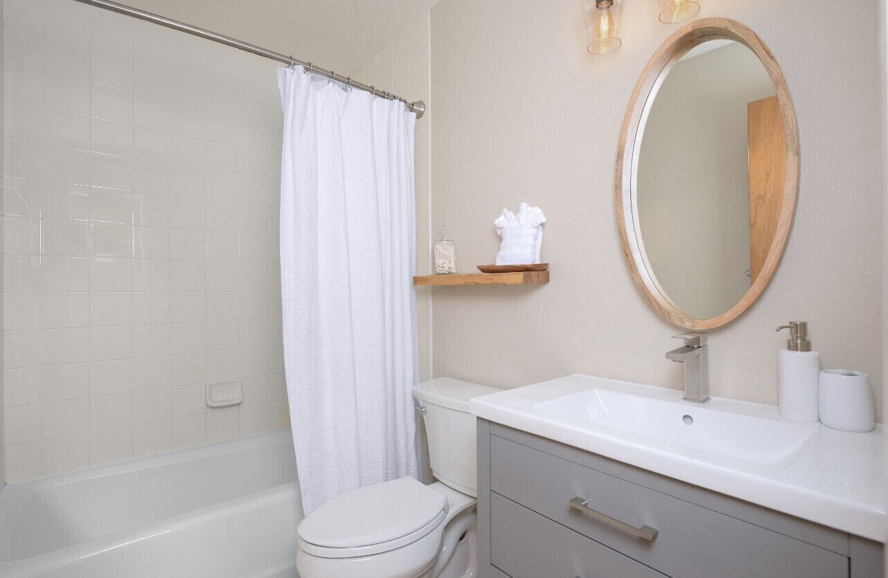 A bathroom with a bathtub, toilet, and vanity with a mirror.