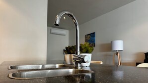 Una cocina con un lavamanos de acero inoxidable, una olla blanca con una planta y una lámpara blanca sobre un pedestal.