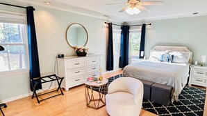 Quarto com cama, mesas de cabeceira, cômoda, cadeira, espelho e ventilador de teto.