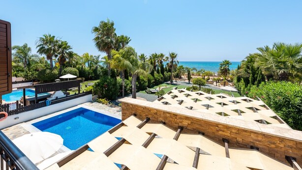 A rooftop pool area with a view of the sea, surrounded by palm trees and lounge chairs.