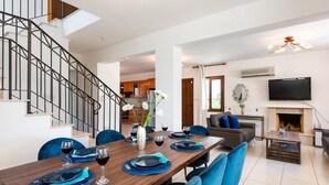 A modern living room with a dining area, a staircase, and a fireplace.