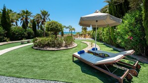 A well-maintained garden with artificial grass, a lounge chair, and an umbrella.