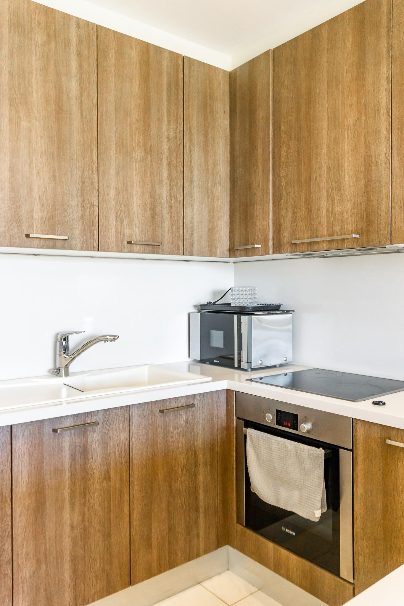 A modern kitchen with wooden cabinets, a stainless steel sink, a microwave, and a Bosch oven.