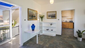 A modern interior with a white wall, a blue vase on a white table, and a kitchen in the background. - Lordos Sunshore Beachfront Suite (Larnaca)