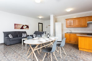 A modern kitchen with wooden cabinets, a dining area with a table set for four, and a gray sofa with patterned cushions.