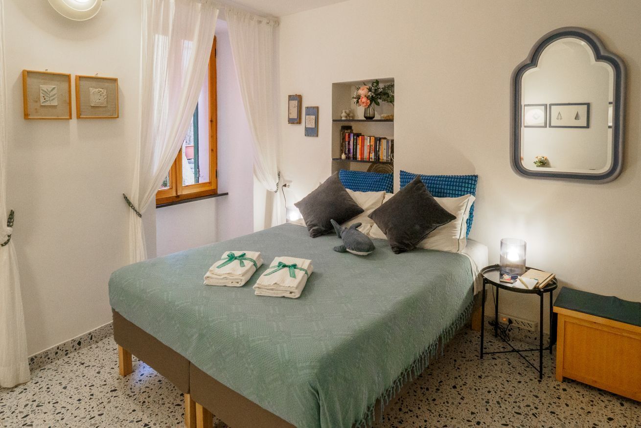 A neatly arranged bedroom with a bed, pillows, a bedside table, a mirror, and a bookshelf.