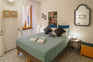 A neatly arranged bedroom with a bed, pillows, a bedside table, a mirror, and a bookshelf. - Rissu Nice Studio in Vernazza (Vernazza)