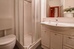 A bathroom with a toilet, a shower enclosure, a sink with a mirror, and cabinets. - Rissu Nice Studio in Vernazza (Vernazza)