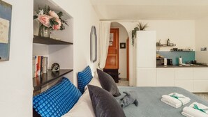 A bedroom with a bed, pillows, a bedside table, a mirror, a shelf with books, a vase with flowers, and a view into the kitchen. - Rissu Nice Studio in Vernazza (Vernazza)