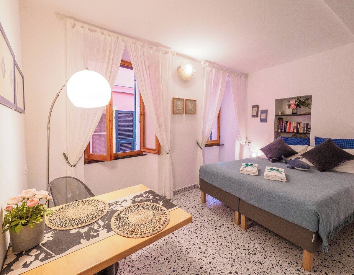 A bedroom with a bed, bedside table, lamp, curtains, and a window with shutters.