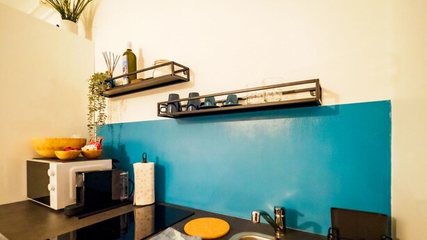 A kitchen with a blue accent wall, a microwave, a sink, and shelves with kitchenware. - Rissu Nice Studio in Vernazza (Vernazza)