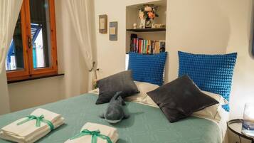 A hotel room with a bed, pillows, a bookshelf, and a window with curtains.