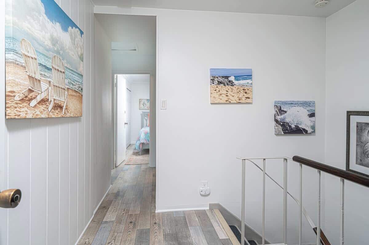 Un couloir doté d’un plancher en bois, de murs blancs et d’œuvres d’art représentant des scènes de plage.