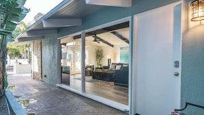A modern house with a patio area, a sliding glass door leading to a living room with a sofa and a coffee table, and a small outdoor seating area. - Newport Beach Balboa House with Large Patio, Walk to Lido Village (Newport Beach)