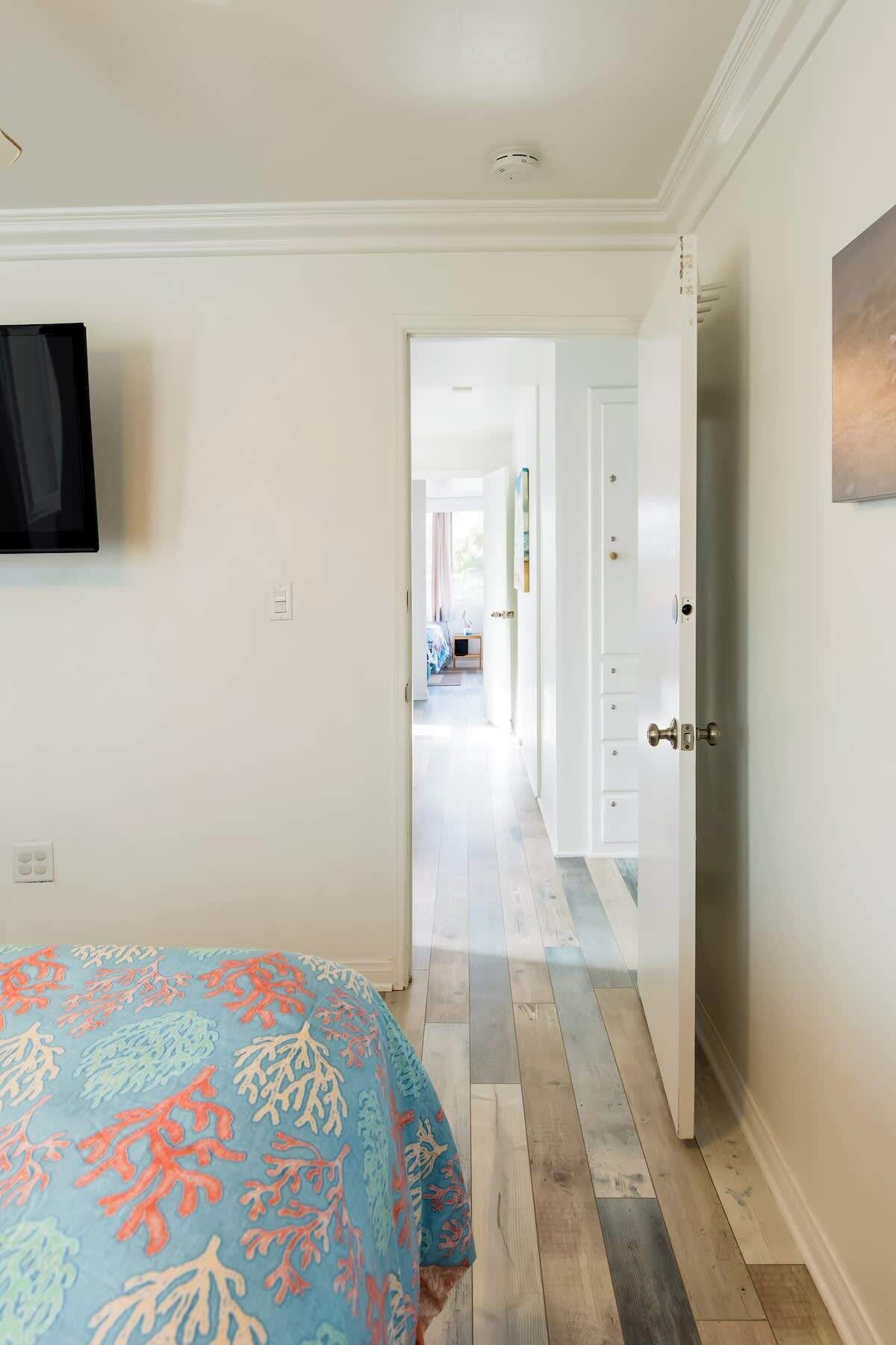A bedroom with a bed, a TV mounted on the wall, and a hallway leading to another room.