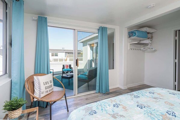 Une chambre avec un grand lit, un fauteuil avec un coussin, une petite table et une vue sur le balcon extérieur.