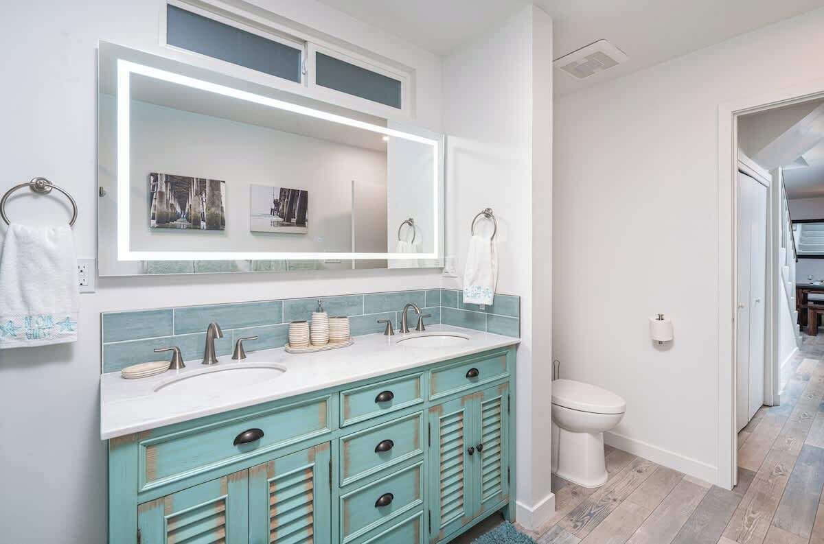 A bathroom with a double sink vanity, a large mirror, and a toilet.