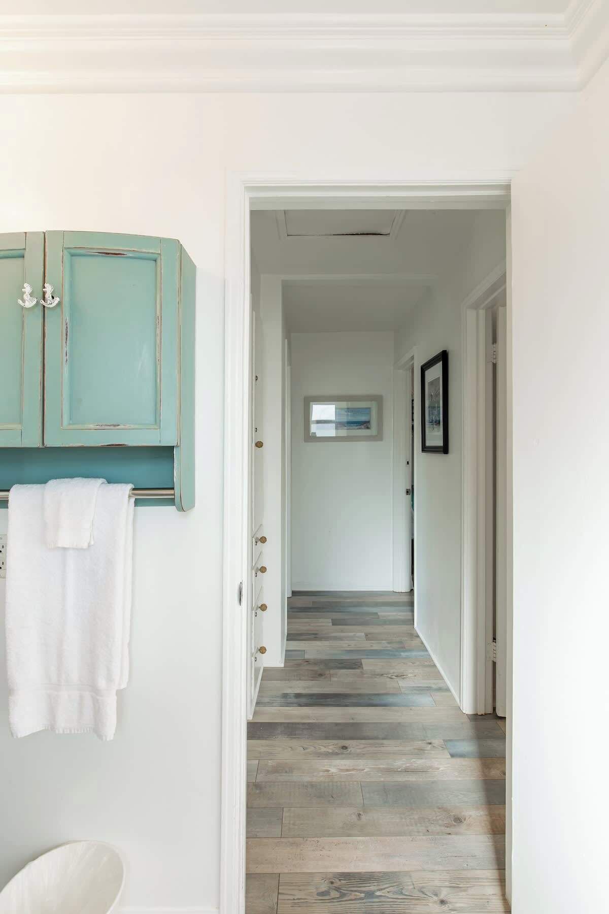 Un couloir avec un plancher en bois, des murs blancs et un meuble turquoise sur lequel est accrochée une serviette.