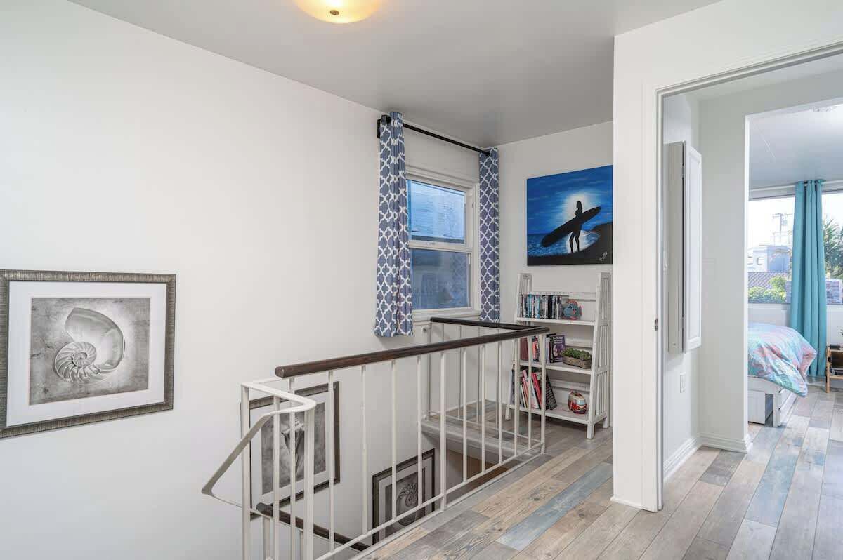 A staircase with a white railing leading to a landing. There is a framed picture on the wall and a bookshelf with books and decorative items.