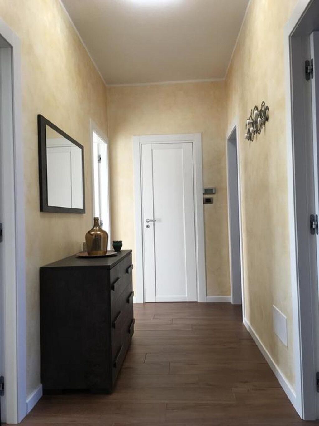 A hallway with beige walls, a dark wooden dresser, a white door, and a small decorative item on the wall.