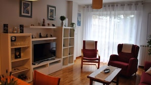 Una sala de estar con televisor, muebles de madera, un sillón rojo y una mesa con camino de mesa.