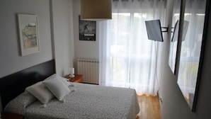 Un dormitorio con cama, mesita de noche, radiador, ventana con cortinas y un cartel en la pared.