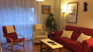 Una sala de estar con un sofá rojo, un sillón rojo, un sillón color beige, una mesa de centro de madera y una lámpara de pie.