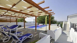 Ein Poolbereich auf dem Dach mit Liegestühlen, einer Pergola und Blick auf das Meer.
