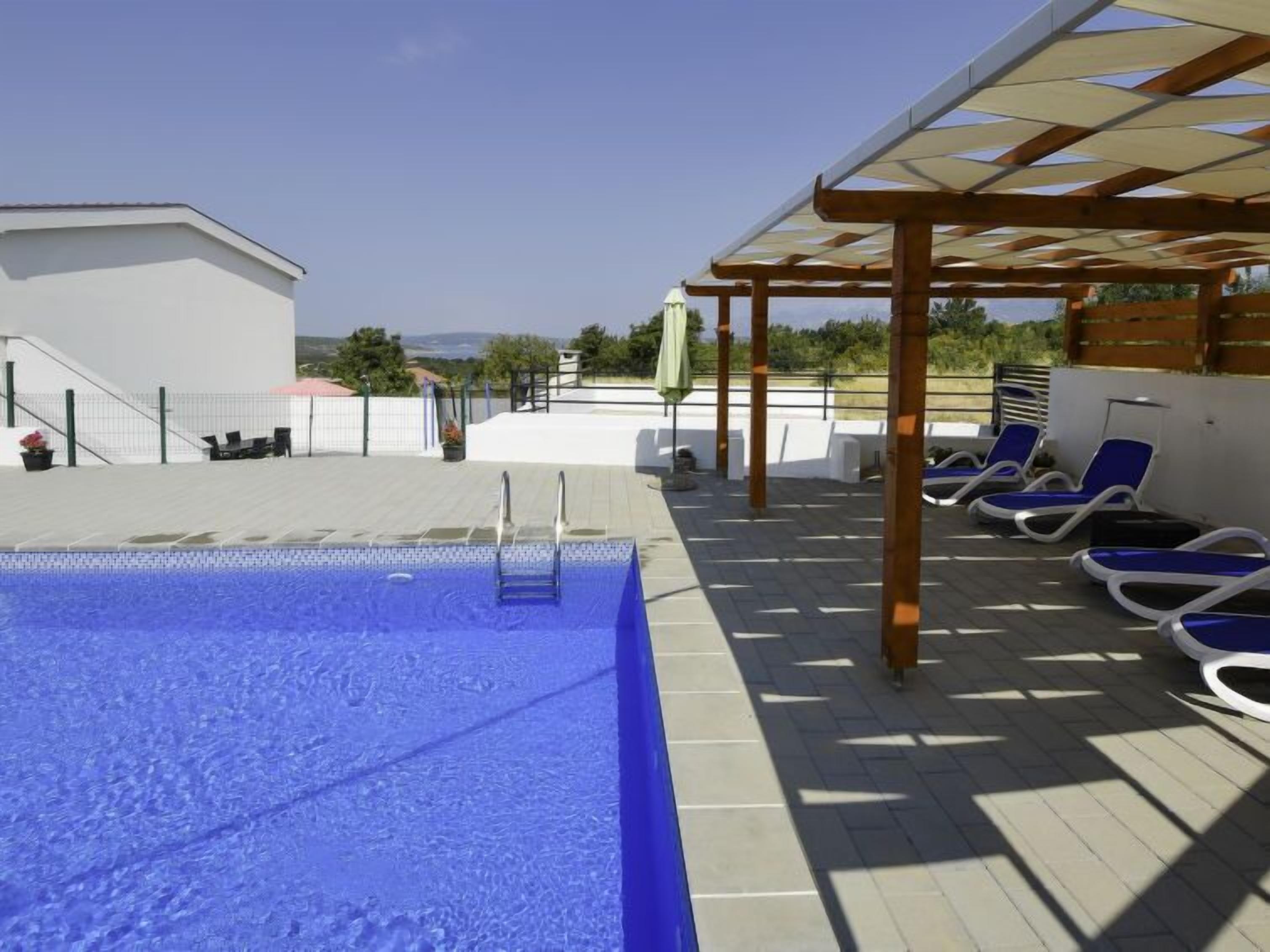 Une piscine à l’eau d’un bleu cristallin, entourée d’une terrasse carrelée et de chaises longues.