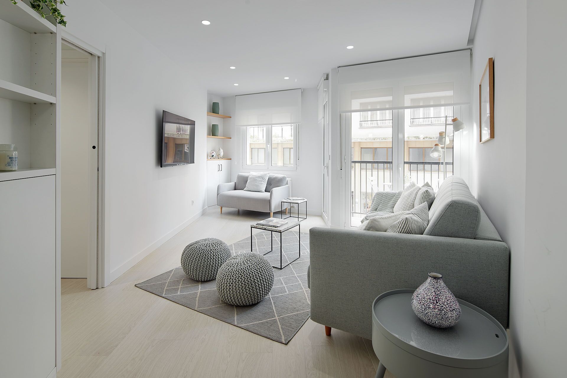 A modern living room with a grey sofa, a coffee table, and a grey rug. There is a window with a view of buildings outside.
