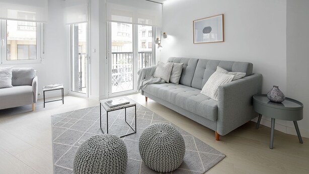 En moderne stue med en grå sofa, en lille rund puf, et sofabord og et billede i ramme på væggen.