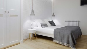 A modern bedroom with a white bed, grey pendant lights, and a white brick wall. - Marugame by FeelFree Rentals (San Sebastián)