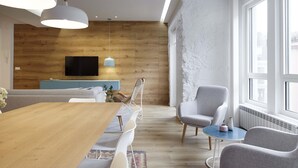 A modern living room with a wooden floor, a wooden wall, a TV mounted on the wall, a dining table with chairs, and a large window providing natural light. - Marugame by FeelFree Rentals (San Sebastián)