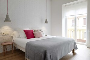 A bedroom with a bed, two pendant lights, a small wooden stool, and a white brick wall.