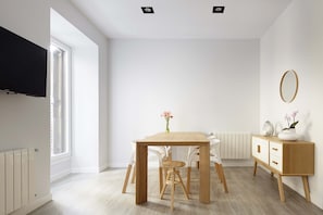 A modern, well-lit dining area with a wooden table, white chairs, and a white cabinet with a mirror.